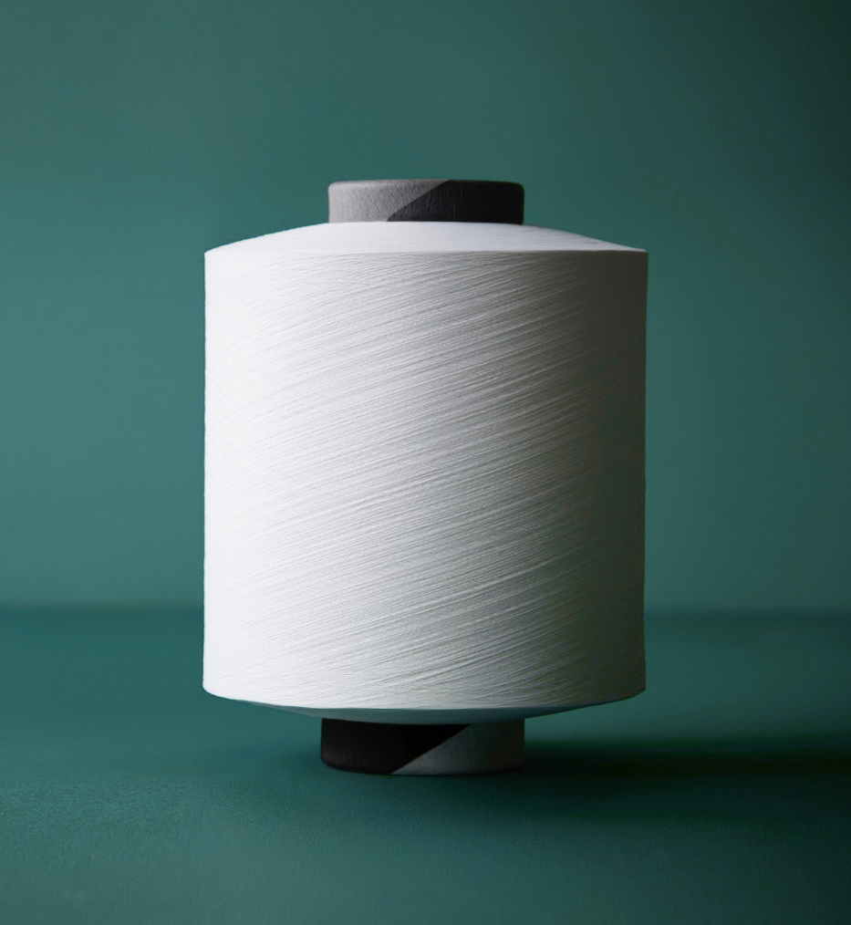 White spool of yarn stands upright against a teal background, featuring a dark grey top and a black and grey base.