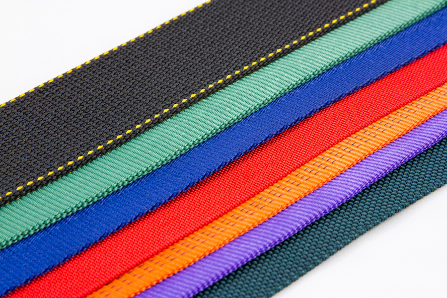 Nylon straps arranged horizontally, featuring black, green, blue, red, orange and purple textures with yellow stitching detail.