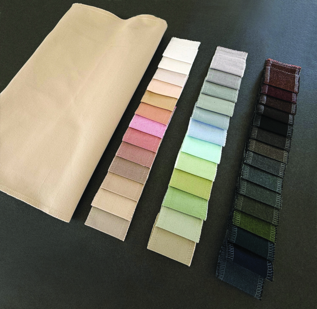 A folded beige fabric swatch next to rows of color samples in pastel and darker shades, all displayed on a dark background.