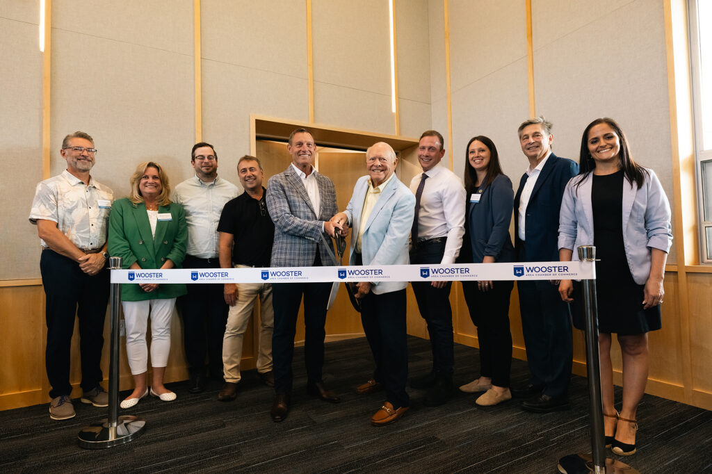 A group of individuals stands together, smiling and holding scissors in front of a blue ribbon, celebrating a grand opening event.