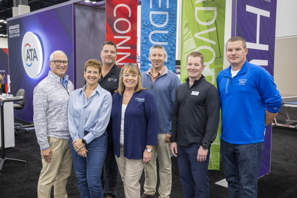 Group of seven individuals at an event, standing together in front of colorful banners, displaying a mix of casual and professional attire.